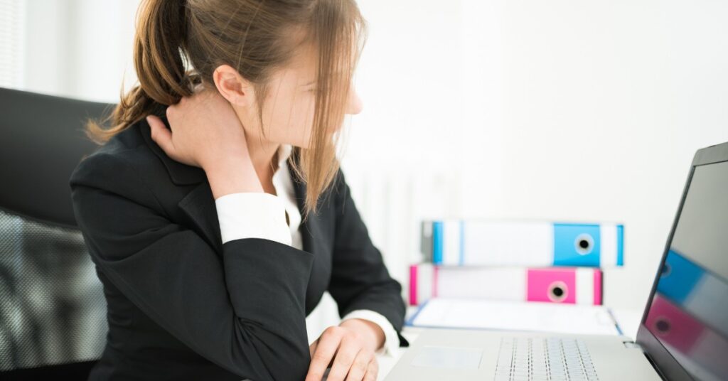 Business Woman Sitting At Work Desk With Poor Posture Grabbing Her Neck Indicating Neck Pain or Headaches | St. Johns Chiropractic & Performance